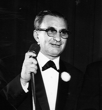 old photo of man in suit holding a microphone